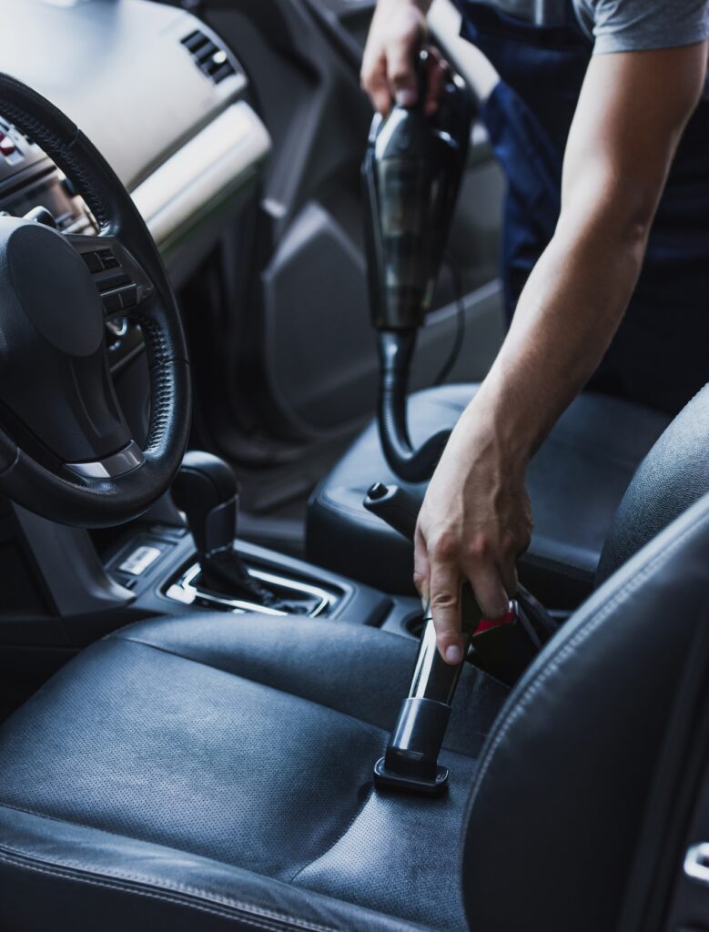 partial view of car cleaner vacuuming drivers seat in car